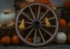 Rustic autumn display featuring pumpkins and a wooden wagon wheel on hay bales, perfect for fall decor inspiration.